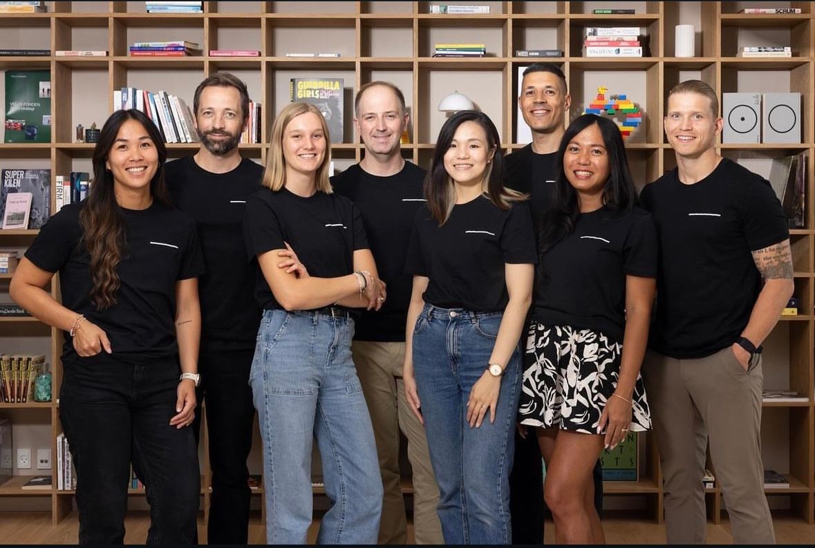 Group of people wearing black shirts standing in front of a bookshelf filled with books and various items.