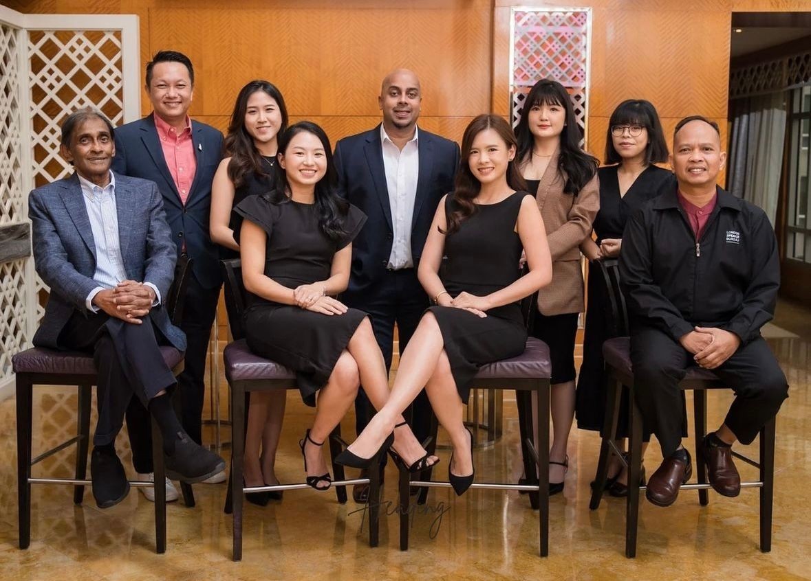 Group of eight people posing for a formal photo indoors, some seated and others standing behind.